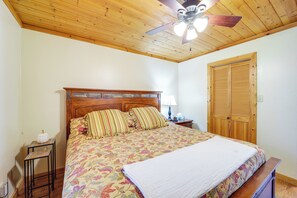 Un dormitorio con techo de madera, una cama con ropa de cama floral, una mesita de noche con una lámpara y un armario de madera.