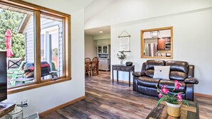 A living room with a leather couch, a coffee table with a plant, and a view of the backyard through a large window. - Family Home w/ Deck, Yard, Dock on Rock River (Janesville)