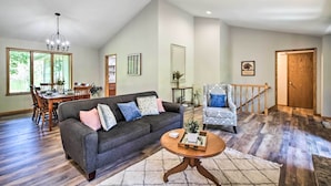 A spacious living room with a dark grey sofa, a patterned armchair, and a dining area with wooden furniture. - Family Home w/ Deck, Yard, Dock on Rock River (Janesville)