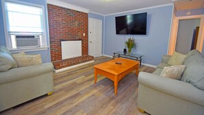 A living room with two sofas, a coffee table, a brick fireplace, a TV mounted on the wall, and a window with blinds. - Holiday Cottage-Oceanside 77th St, W/D, AC, Free WIFI (Ocean City)