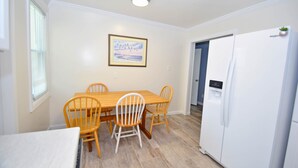 A dining area with a wooden table and chairs, a white refrigerator, and a framed picture on the wall. - Holiday Cottage-Oceanside 77th St, W/D, AC, Free WIFI (Ocean City)