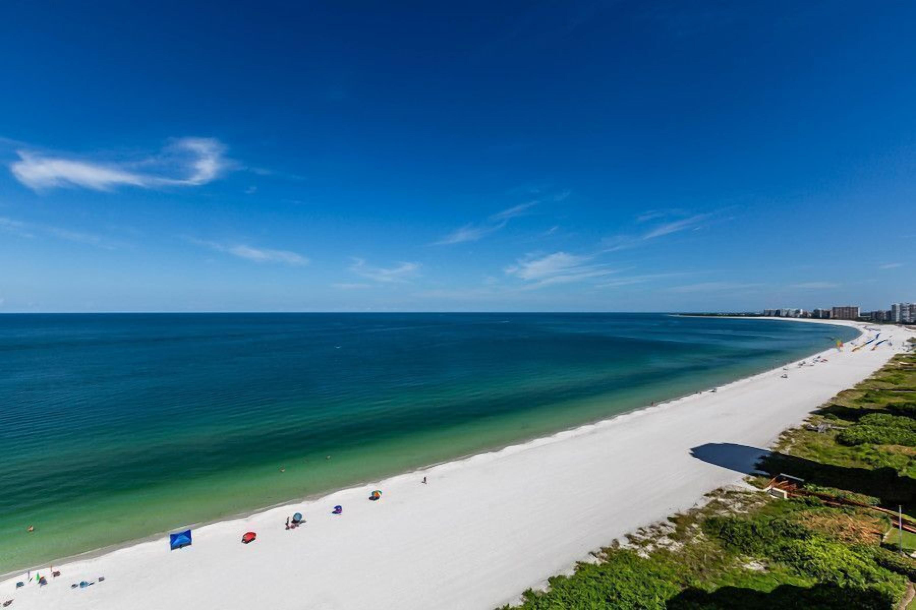 Ein Strand mit weißem Sand, klarem türkisblauem Wasser und einigen Sonnenschirmen.