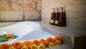 Une baignoire avec un mur en pierre en arrière-plan, une étagère en bois où sont posés des produits de bain et des fleurs de souci.