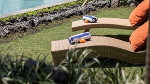 Un espace aménagé au bord de la piscine, avec des fauteuils de relaxation en osier, un fauteuil suspendu et une pergola en bois.