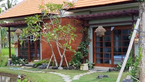 Une maison avec une façade en briques, un toit en tuiles et un jardin agrémenté d’un bassin, de pas japonais et de plantes.