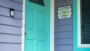A turquoise door with a welcome sign, a small gnome figure, and a doormat.