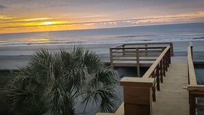 A wooden boardwalk leading to the beach with a palm tree in the foreground.