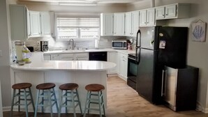 A modern kitchen with white cabinets, a central island with stools, a refrigerator, and a microwave.