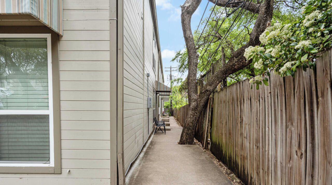 A narrow pathway between two buildings with a wooden fence on one side and a window on the other.