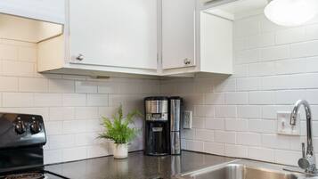 A kitchen with white cabinets, a black stove, a coffee maker, and a sink.