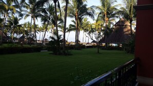 A well-maintained lawn with palm trees and thatched-roof structures, suggesting a tropical resort setting.