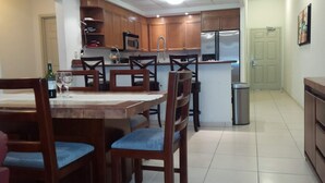 A kitchen with wooden cabinets, a stainless steel refrigerator, and a dining area with wooden chairs and a table.