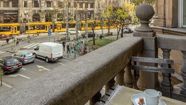 En balkon med udsigt over en historisk bygning, en sporvogn og et gadesceneri.