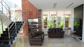 A modern living room with a staircase, leather sofas, and a glass display case. - Nacional Hotel Jataí (Jatai)