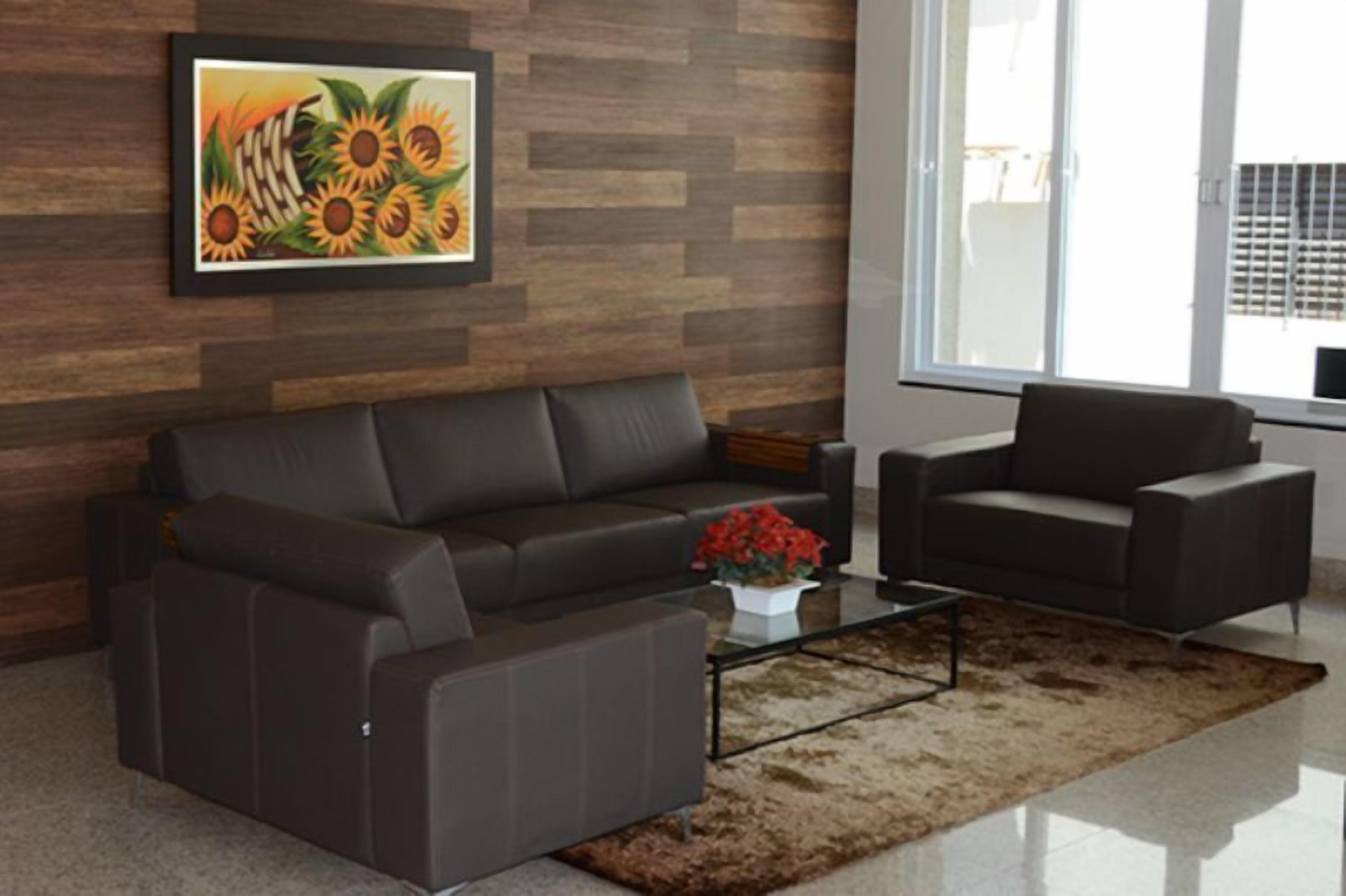 A modern living room with a dark brown leather sofa, a black armchair, and a coffee table. There is a framed painting of sunflowers on the wall.