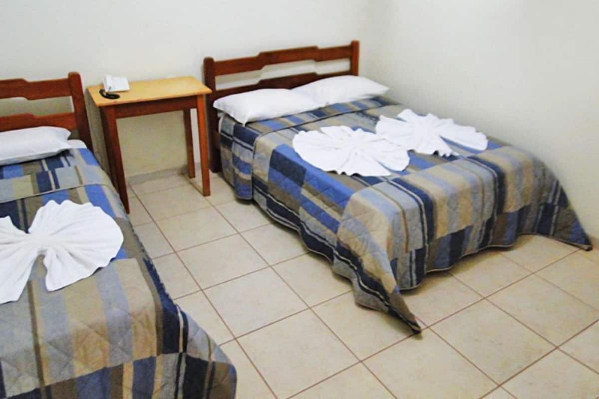 Een hotelkamer met twee enkele bedden, elk voorzien van een geruit sprei en een witte handdoek. Daartussen staat een houten nachtkastje met een telefoon en een klein tafeltje.