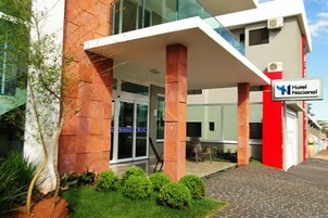 Um hotel moderno com fachada em vermelho e branco, entrada coberta e placa indicando ser um hotel nacional.