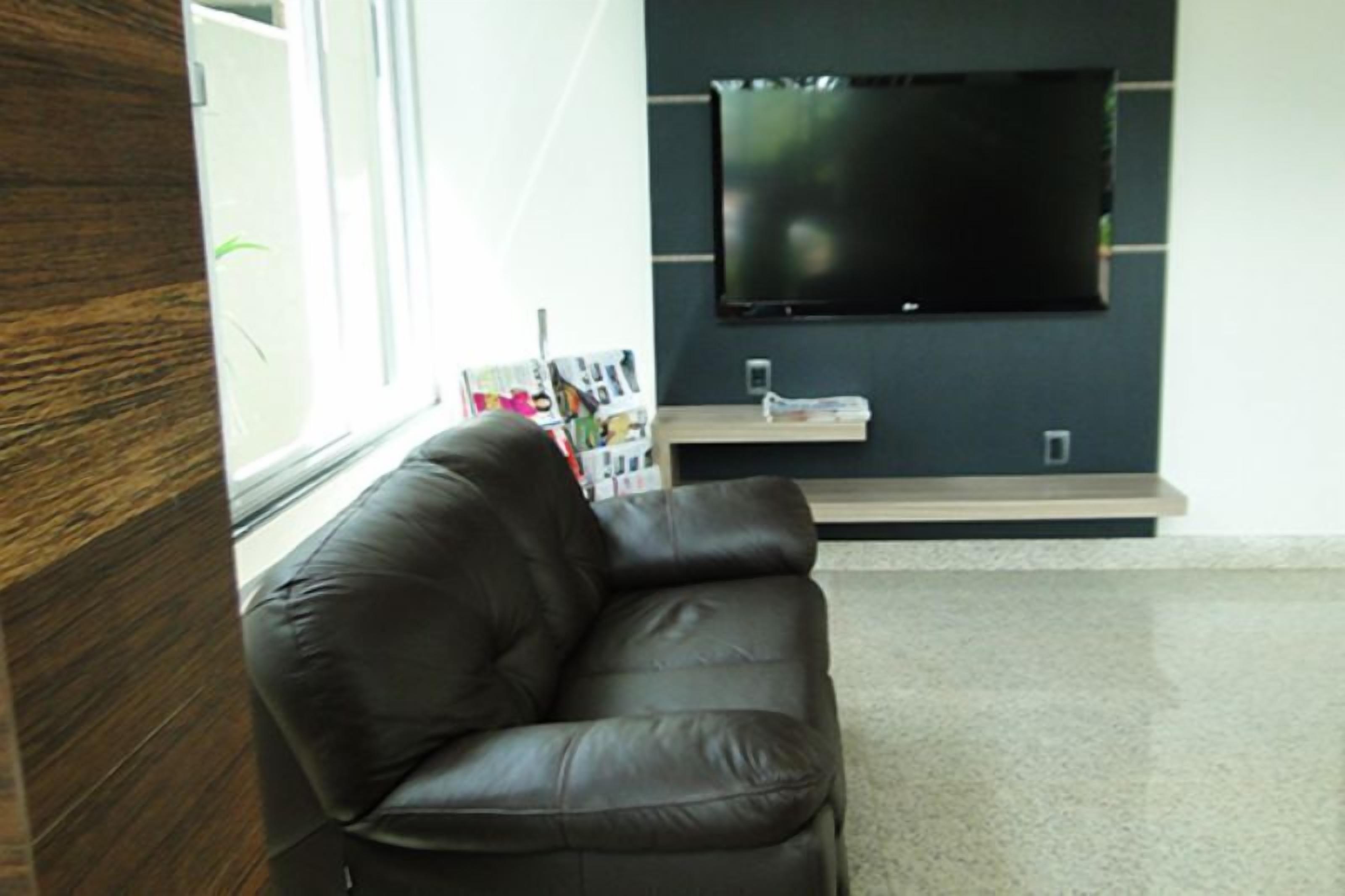 A modern living room with a leather sofa, a flat-screen TV mounted on the wall, and a window with magazines on the windowsill.