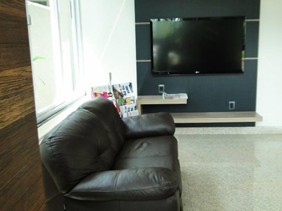 A modern living room with a leather sofa, a flat-screen TV mounted on the wall, and a window with magazines on the windowsill.