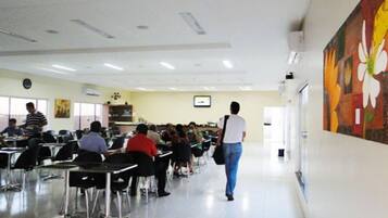 Un aula con filas de escritorios y sillas, un reloj en la pared y un cuadro grande en la pared.