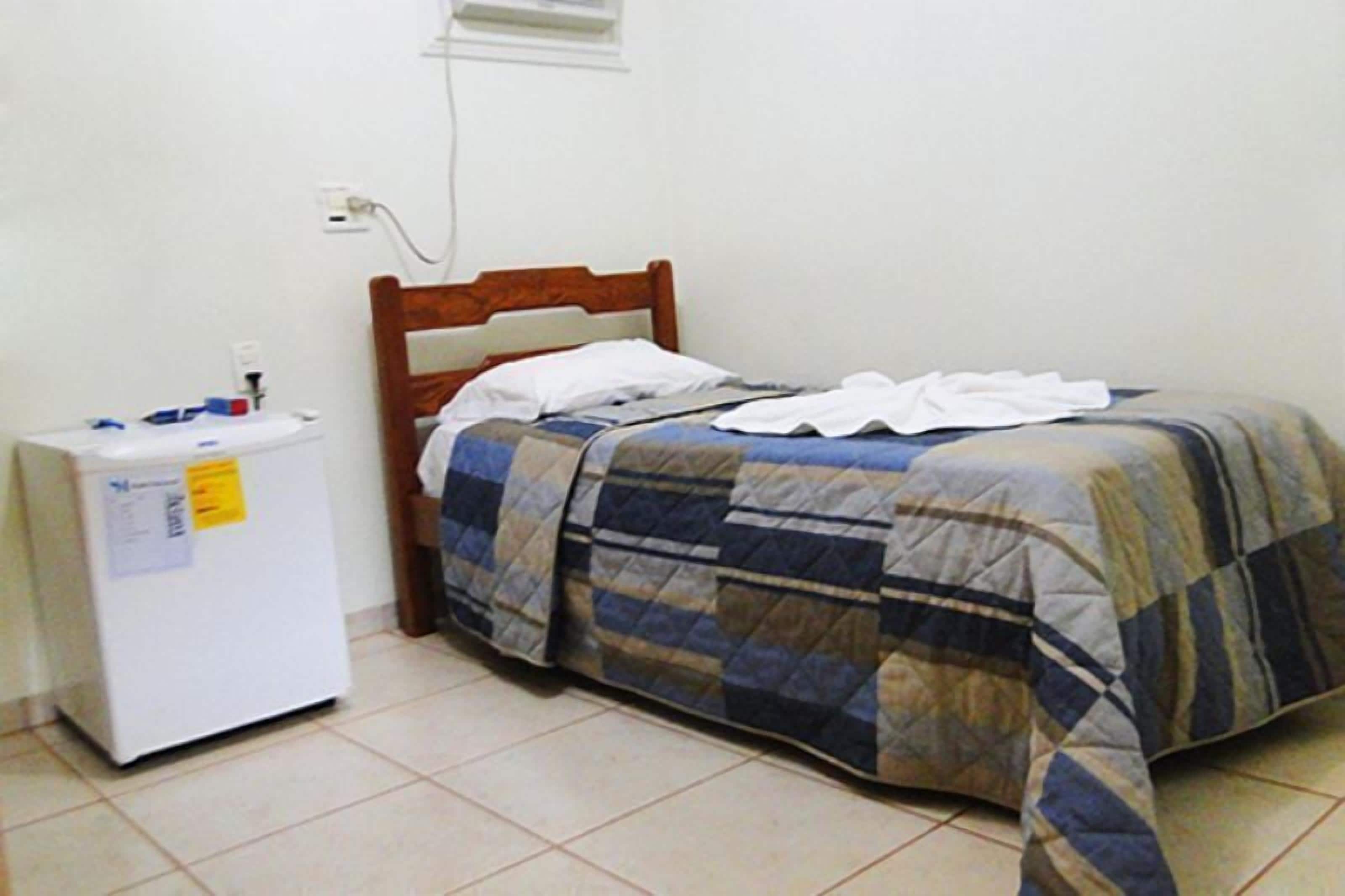 Una habitación pequeña y sencilla con cama, mesita de noche y refrigerador.