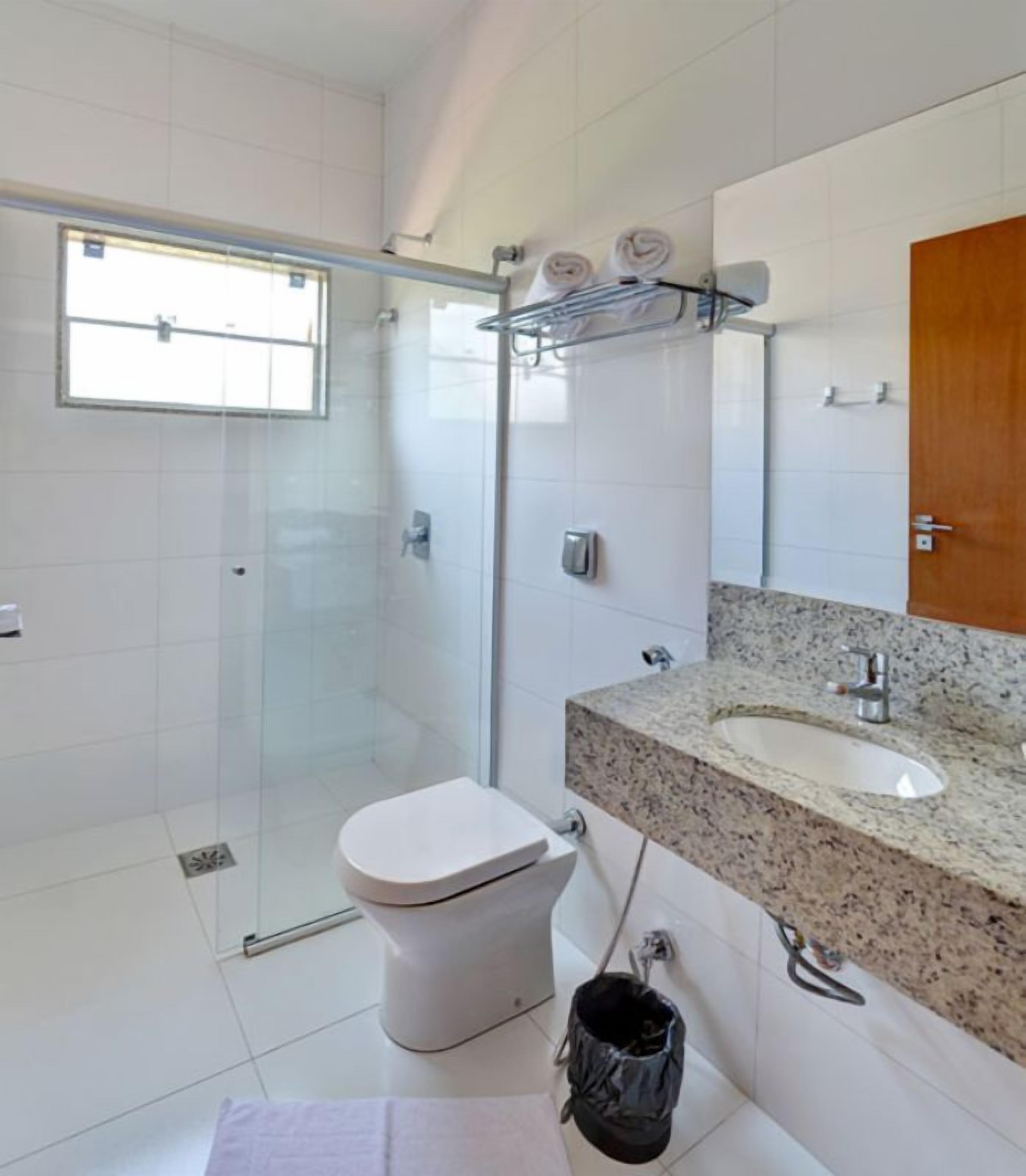 Un baño moderno con cabina de ducha de vidrio, inodoro blanco, lavamanos con encimera de granito y puerta de madera.