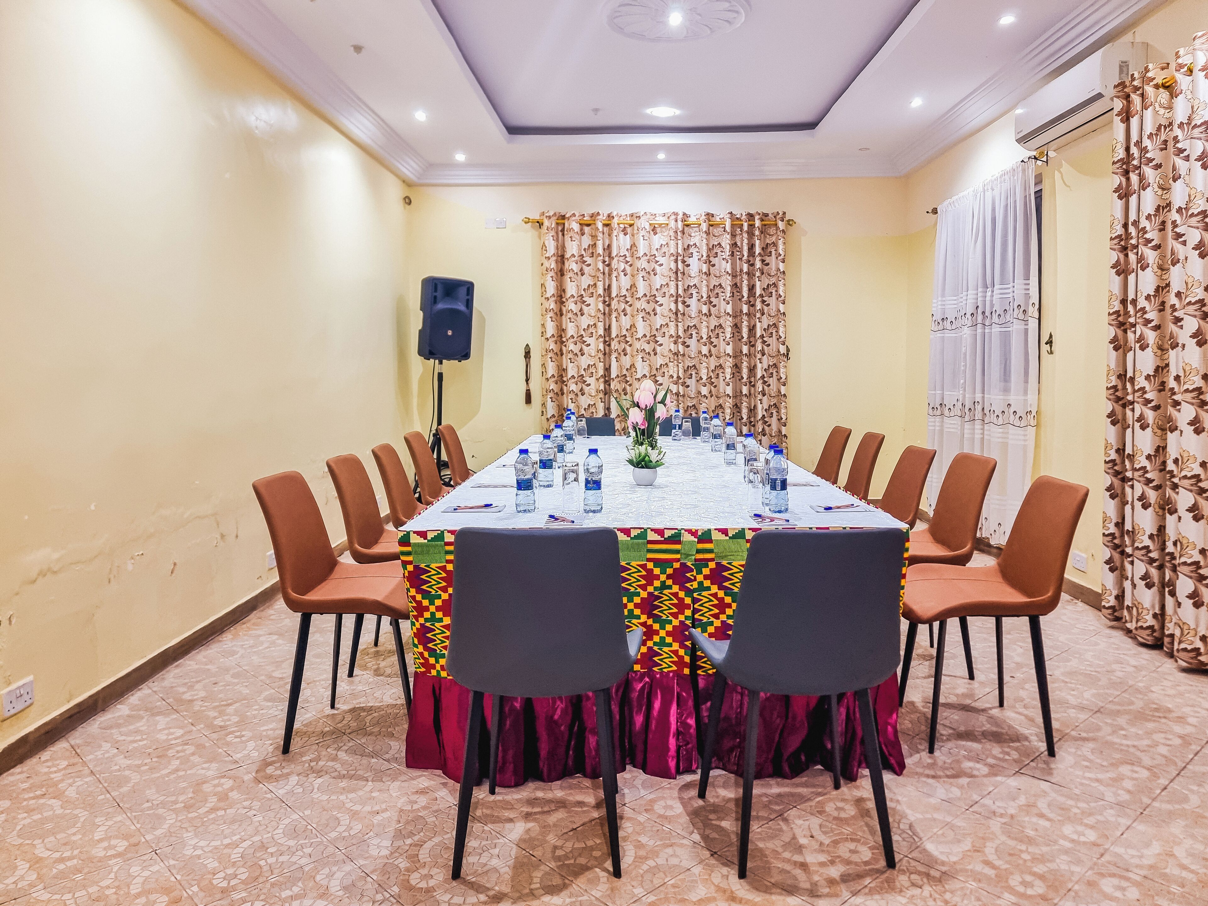 A conference room with a long table, chairs, a speaker, and a potted plant.