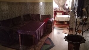 A living room with a sofa, a dining table, and a television. - Chez Simo un petit coin de relax (Safi)