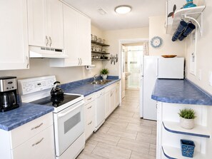 A modern kitchen with white cabinets, a stove, a kettle, and a coffee maker.