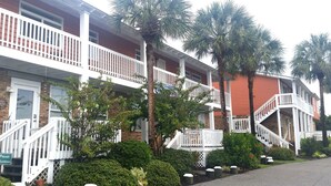 Un hotel de varios pisos con barandas blancas, palmeras y fachada de ladrillo.