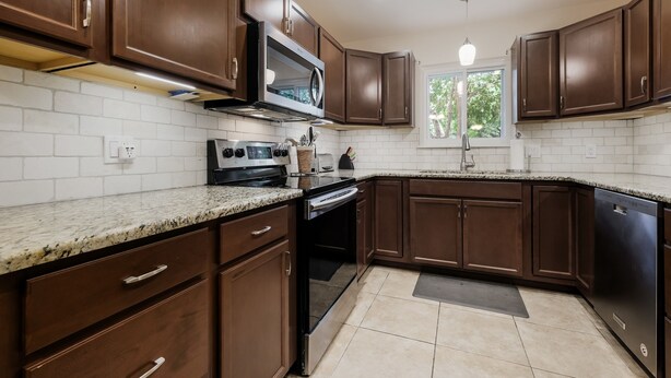 A modern kitchen with dark wooden cabinets, a stainless steel oven, and a granite countertop. - Sage Suite II - Safe, Cozy & Pet Friendly. (San Antonio)