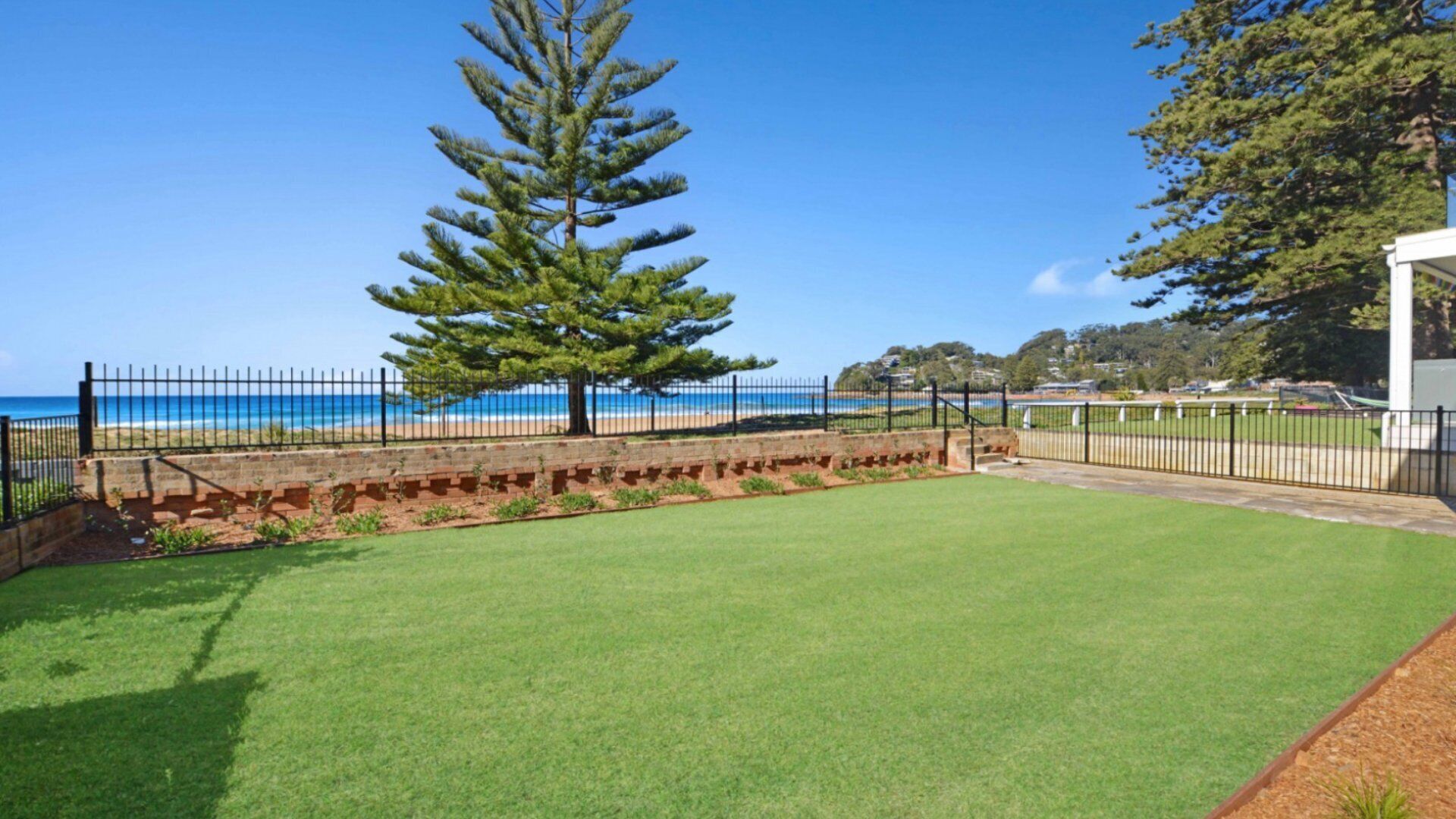 A grassy area with a fence, a tree, and a view of the beach and ocean.
