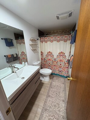 Une salle de bain avec un lavabo blanc, des toilettes et un rideau de douche à motifs floraux.