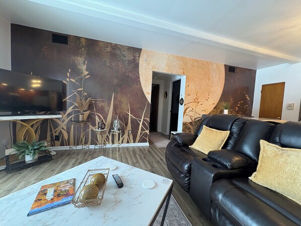 Un salon moderne avec un canapé en cuir, un téléviseur à écran plat, une table basse agrémentée d’objets décoratifs et un mur au motif texturé.