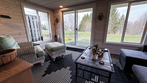 A cozy room with wicker furniture, a black and white striped rug, and a view of a grassy yard through large windows. - Country Apartment Rental in an Outdoor Paradise! (Mt Carroll)