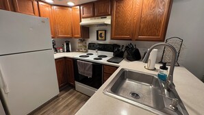 A compact kitchen with wooden cabinets, a white refrigerator, a stove, and a sink. - Country Apartment Rental in an Outdoor Paradise! (Mt Carroll)