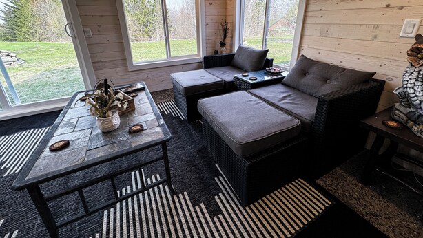 A cozy room with a sofa, a coffee table, and a wicker chair. There are large windows and a view of the outdoors. - Country Apartment Rental in an Outdoor Paradise! (Mt Carroll)