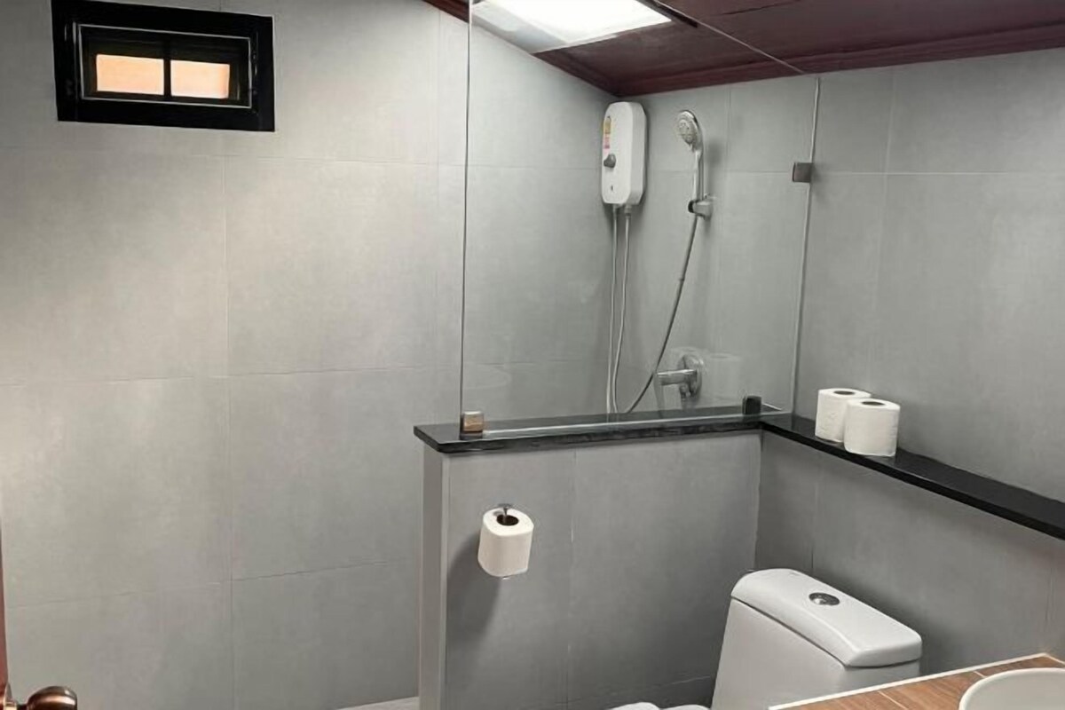 A bathroom with a toilet, a shower, and a shelf with toilet paper.
