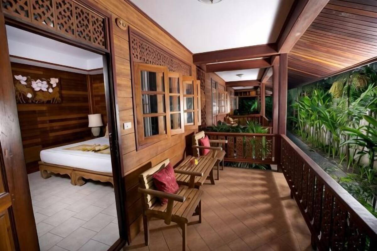 A wooden room with a bed, a bench, and a view of greenery through a window.