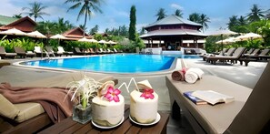 Un espace aménagé au bord de la piscine, avec des chaises longues, une piscine et un bâtiment doté d’un toit remarquable.