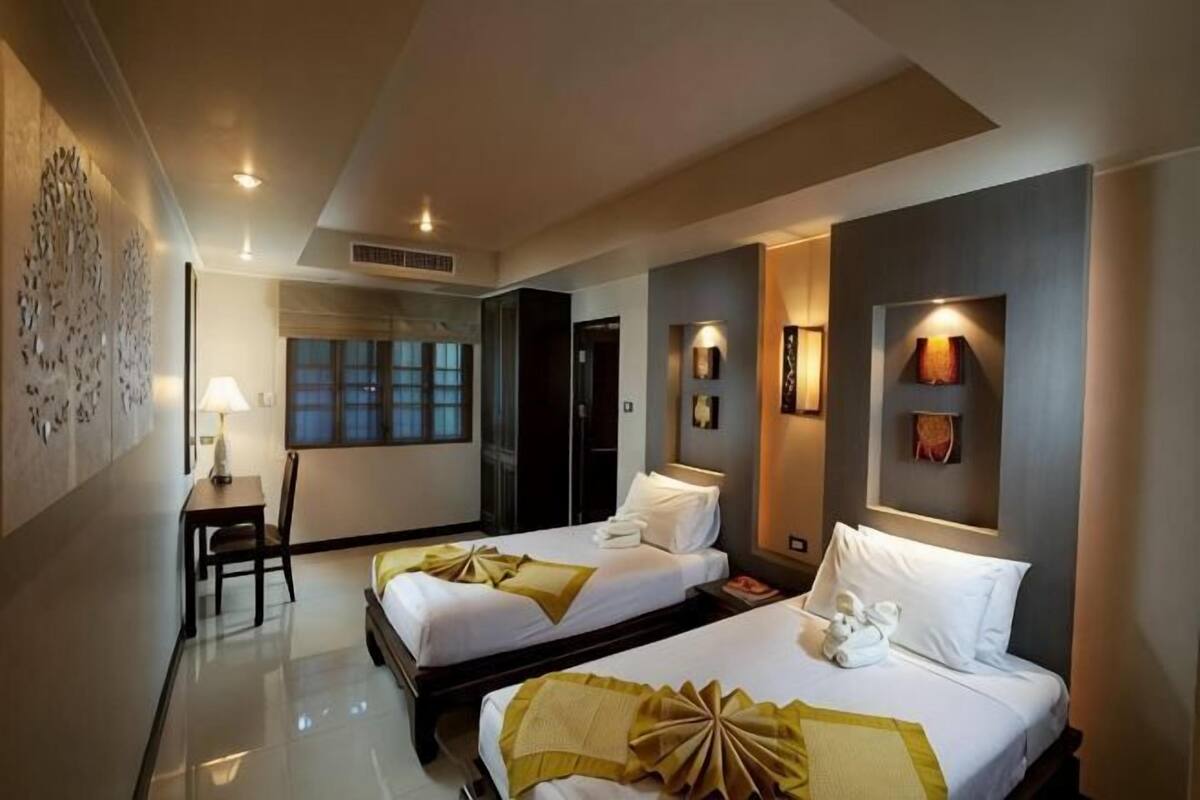 A hotel room with two beds, a desk, a chair, and a window.