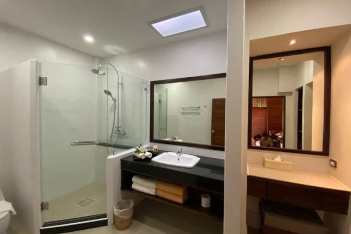 Un baño moderno con ducha envuelta en vidrio, lavamanos blanco y un espejo grande.