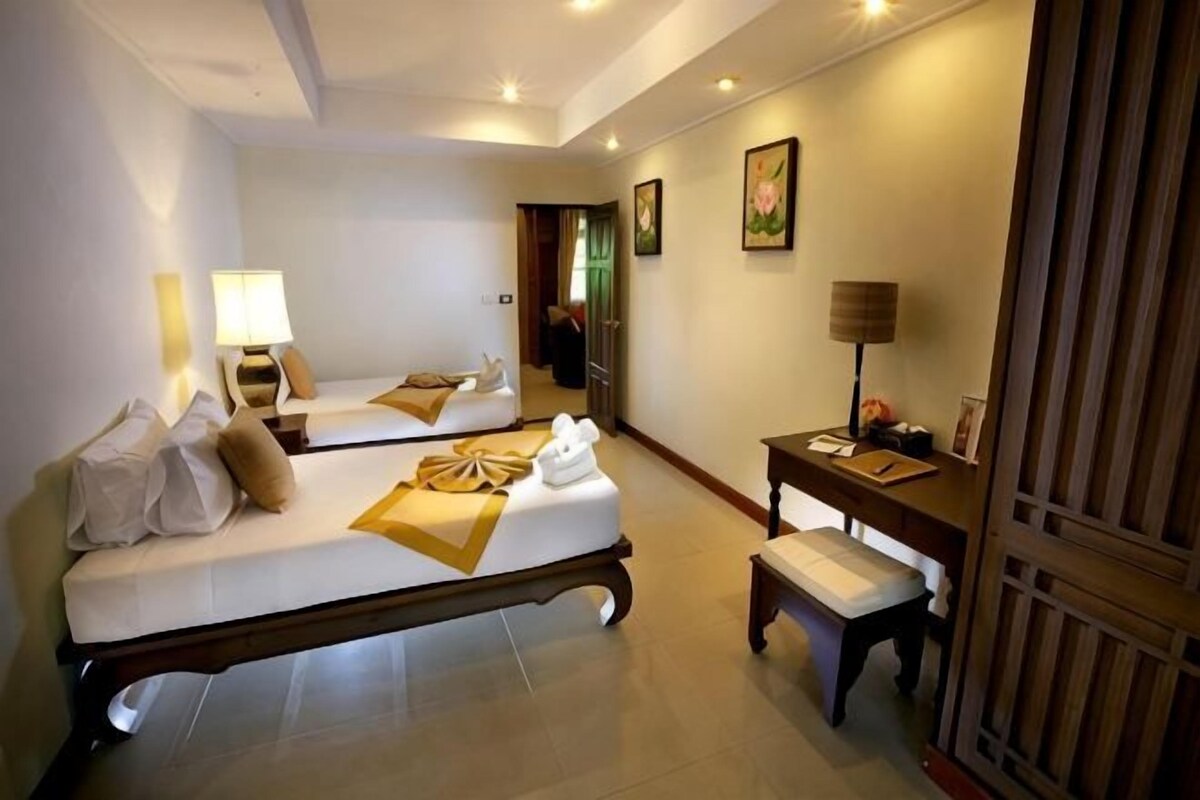 A hotel room with two beds, a desk, a chair, a lamp, and a mirror.