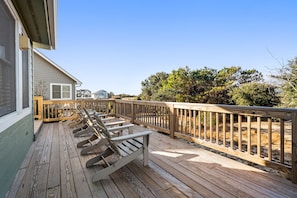 A wooden deck with lounge chairs, a railing, and a view of a house and trees.