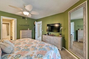 A bedroom with a bed, dresser, mirror, ceiling fan, and a wall-mounted TV. - Resort Condo w/ Beach Access on Anna Maria Island! (Bradenton Beach)