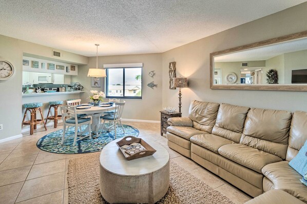 A living room with a beige leather sofa, a round coffee table, and a dining area with a blue patterned rug. - Resort Condo w/ Beach Access on Anna Maria Island! (Bradenton Beach)