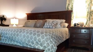 A neatly made bed with patterned bedding, a wooden headboard, a bedside table with a lamp, and a nightstand with a decorative item. - A Clean, Safe, House full of steel balls & vintage game consoles (Richmond)