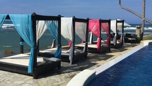 A poolside area with four sunbeds, each with a canopy, overlooking the ocean. - BEACHFRONT STUDIO APARTMENT WITH GREAT VIEW OF THE OCEAN. (Cabarete)