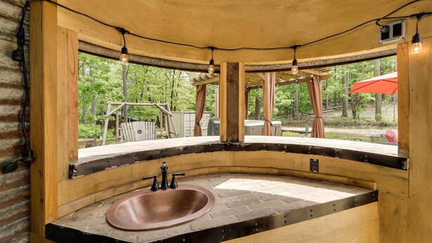 A rustic bathroom with a curved stone sink, wooden beams, and a view of the outdoors.