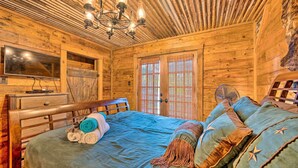 A wooden cabin room with a bed, a television, and a large window.